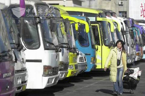 一位回家的旅客经过停靠在汽车站里整装待发的大客车前